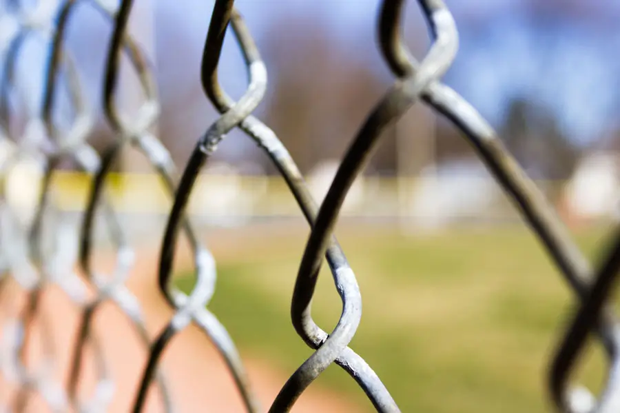 A close-up view of a metal chain link fence with a blurred background of a field, illustrating sturdy fencing materials. Ideal for those searching for chain link fencing Lafayette for security and durability.