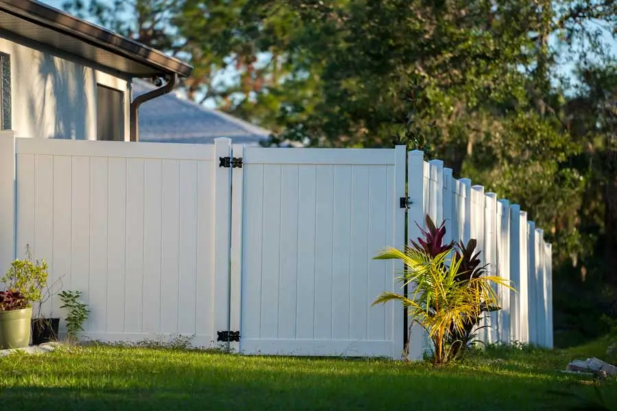 White vinyl fence in a residential backyard with greenery, showcasing a well-maintained structure for vinyl fence repair service