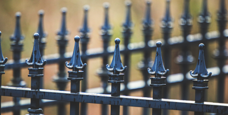 Part of a fence crafted from black wrought iron with pointed decorative finials, arranged in a row to form a formal and stylish boundary.