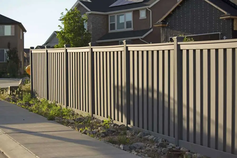 Sturdy, modern vertical-slat privacy fence enclosing a residential area along a clean sidewalk, installed by a professional commercial fence company known for quality and security.